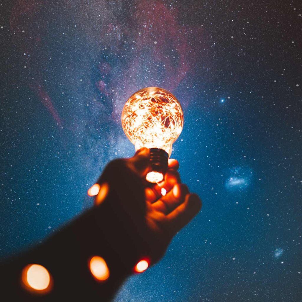 Fractional CMO - A hand holding up a lightbulb into a starry night sky